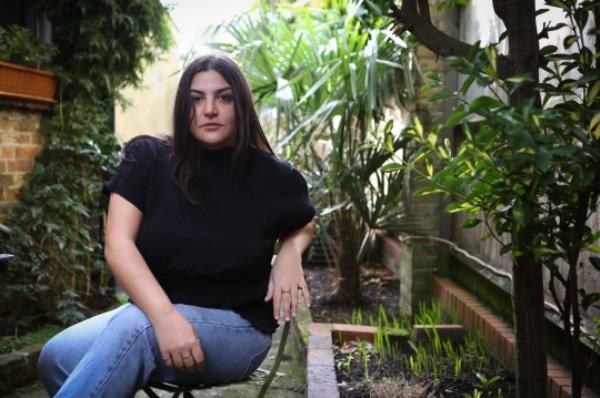 Almara in her garden, on a chair, wearing jeans and a black t-shirt