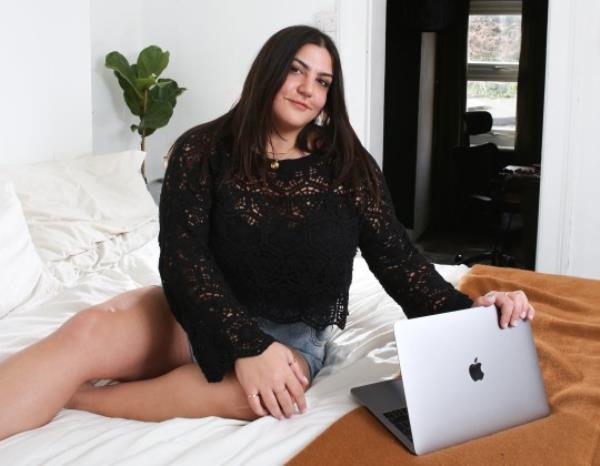 Almara sitting on her bed, with her laptop, wearing a black crocheted top
