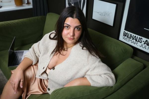 Almara sitting on her green sofa, wearing a gold dress and beige cardigan